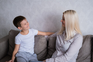 Blonde mom and teen son are sitting on the couch, looking at eac