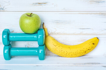 Hand Weights ,Apple and Banana on a White Wooden Background.Fitness Concept 