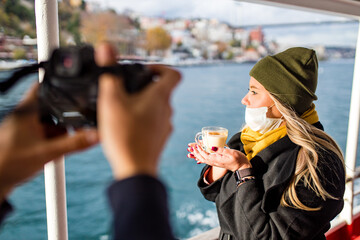 woman drinking hot masala tea in the front, bosphorus bay in the background posing to photographer...