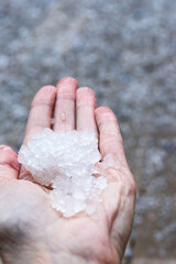 Fototapeta na wymiar Woman is holding pieces ice crystals of hail in springtime after hail storm, defocused ice background, vertical view