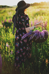 Beautiful woman walking in sunny lupine field with rustic basket and flowers. Tranquil moment