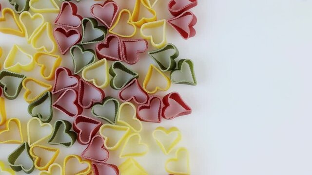 Colored pasta in the form of hearts spinning on a white background. Rotating. Space for text.