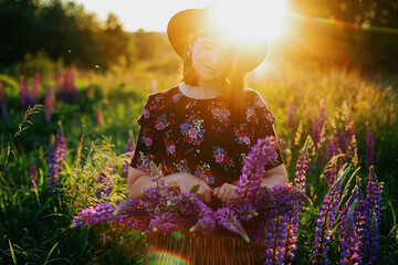 Beautiful woman relaxing in lupine field with rustic basket and flowers at sunset,tranquil moment