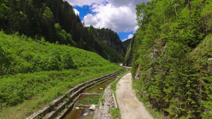Aerial drone view of Lotru river flowing through a narrow canal in a mountainous forested area. Sharp rocky cliffs and crests are narrowing the creek's valley. Carpathian Mountains, Romania.