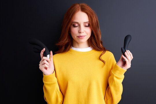 woman likes getting sexual pleasure with vibrator, redhead young female posing with black silicone sex toys, closes eyes and imagines usage of it, exploring your erogenous zones