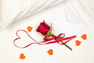 Red heart of ribbon with red rose, envelope and little heart on white bed honeymoon. Surprise Valentine and wedding day in bed. Top view. Copy space.