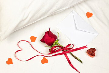 Red heart of ribbon with red rose, envelope, candles, and little heart on white bed honeymoon. Surprise Valentine and wedding day in bed. Top view. Copy space.