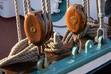 Two brown wooden pulleys with ropes on the side of a ship. Focus on the wood of the pulley at the left