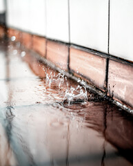 Waterdrop splashes in motion. Rain drops falling on brick tiles in corner. Concept for water leaks or failing or clogged rain pipes. Abstract and defocused rain texture with ripples.