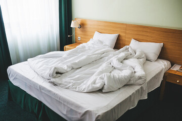 View of a rumpled bed with white pillows and a duvet.