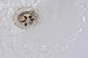 Water drains into the drain hole of the sink. Close-up the concept of waste water and environmental problems, hygiene.