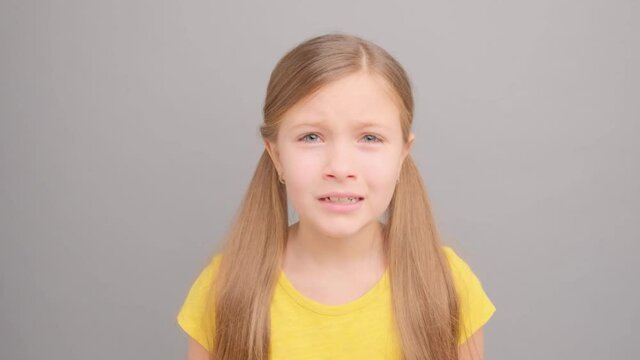 A little girl in a yellow T-shirt is crying and screaming. Picture taken in the studio on a gray background. Close-up portrait of a girl.