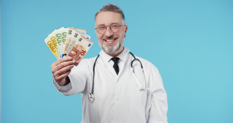 Portrait of smiling male doctor holding in hands euro money isolated over blue background. Euro Money.