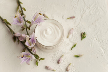 Fototapeta na wymiar White handmade DIY cream in a bottle on a white background with lilac and purple flowers. Natural care for the face, moisturizing and nutrition.