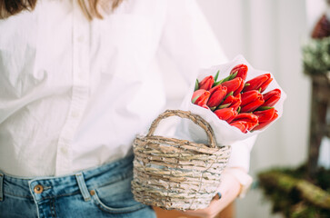 florist woman holding a basket with red tulips in white paper