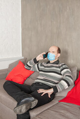 Young man wearing medical mask talking on smartphone at home
