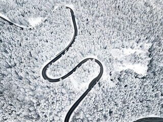 Aerial view of winding road in high mountain pass trough pine woods snowed