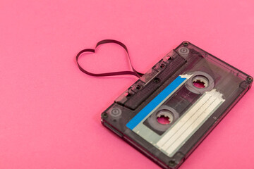 Audio cassette tape on rose backgound. Film shaping heart, Valentine postcard. Empty space.