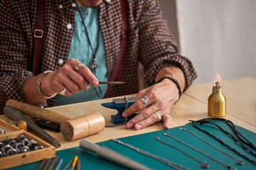 jeweler engaged in delicate jewelry work, working and shaping an unfinished jewelry with a tool in workshop