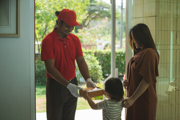 Obraz premium The concept of safe delivery. A courier in a red uniform delivery of orders to mother and little daughter the customer home.