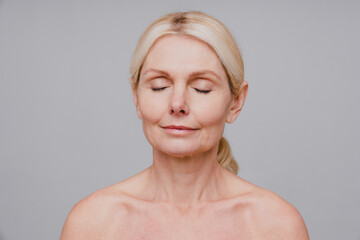 Charming middle-aged woman with closed eyes and fresh clean skin isolated over grey background