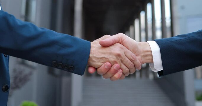 Close up of two Caucasian men shaking hands outdoor at business center. Males businessmen meeting. Meet of partners.