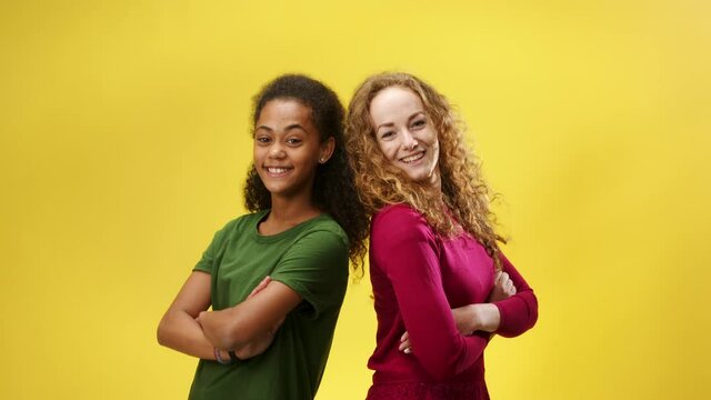 Young woman with teenager girl in a studio on yellow background giving high five then looking at camera.