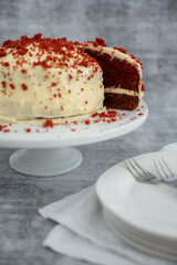 Red velvet cake with plates and cutlery in the foreground and concrete background