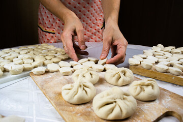 Woman's hands, soiled in flour, neatly lay out handmade, freshly made dumplings, ravioli and khinkali on cutting boards.