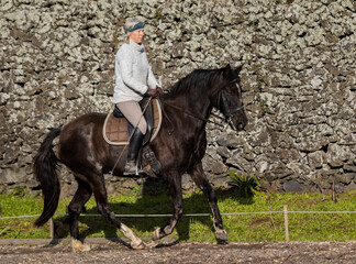 Fototapeta premium Woman riding a black Lusitano horse outdoors, good weather, Azores.