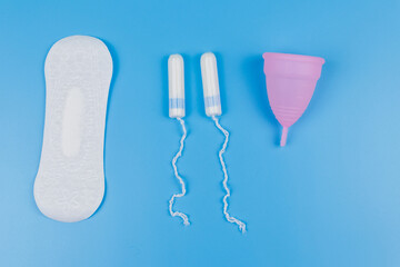 Sanitary pad, tampons and menstrual cup on blue background. Top view. Concept of critical days, menstruation, feminine hygiene