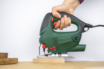 Modern electric jig saw tool in a hand for DIY home woodworking. Wood boards on background