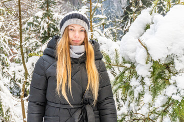 Winter portrait of a beautiful girl in snowy forest. blond woman walking in winter park. The girl looks at the camera
