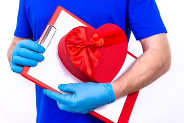 Courier in protective gloves holds red heart-shaped gift box for Valentine's Day. Safe contactless home delivery of gifts to your favorite women on Mother's and Women's Day. love you. Hand close up