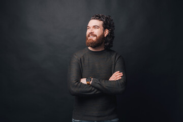 Handsome man with beard and long curly hair standing over dark background with crossed arms and...