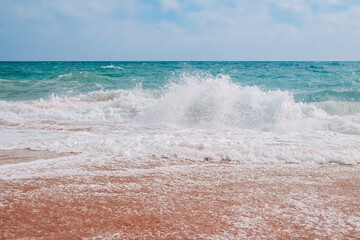 Turquoise waves with foam on the sandy shores of benagil beach in portugal.