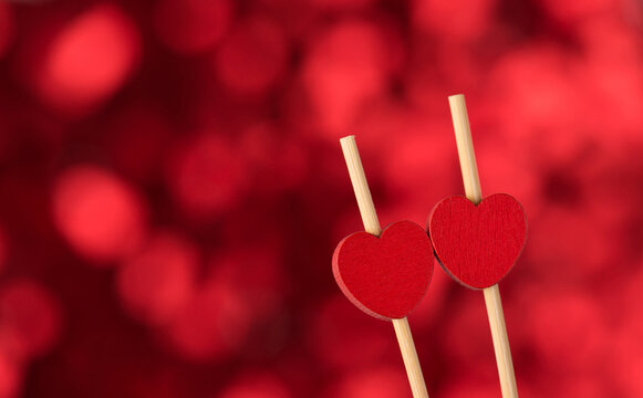 Happy Saint Valentines Day Concept. Close Up Photo Of Two Wooden Heart Shaped Sticks On Red Shimmer Bokeh Backdrop