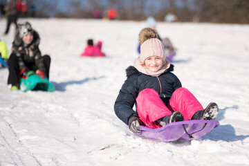 Fototapeta na wymiar Little girl sliding with bob and falling in the snow.