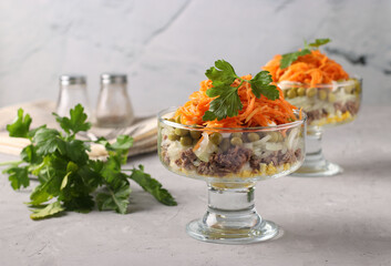 Two servings of salad with Korean carrots, meat and canned peas in transparent salad bowls on a light gray background