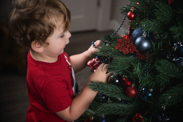Cute little baby decorates the Christmas tree with toys.