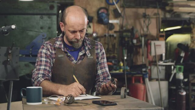 Mature male blacksmith wearing apron working on design in forge - shot in slow motion