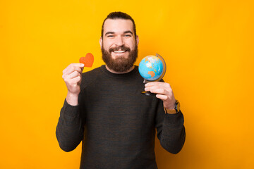 Photo of happy bearded handsome man holding globe and red heart.