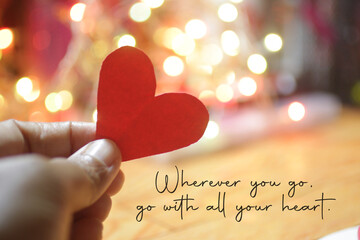 Inspirational quote - Wherever you go, go with all your heart. On pink and white bokeh light background with hand holding red love paper shape. Believe in your heart intuition concept. - obrazy, fototapety, plakaty