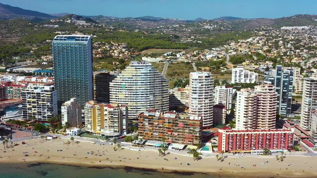 Beach in Spain with the city of calp in the background. We can see tourists walking on the beach with building in the background 4K