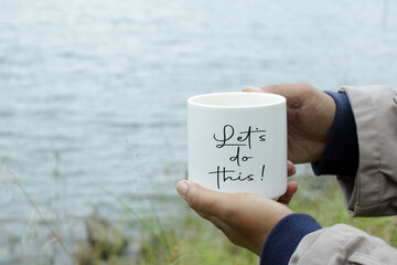 Person holding white cup of tea or coffee in hands with motivational text message on it - Let's do this! Business success concept.