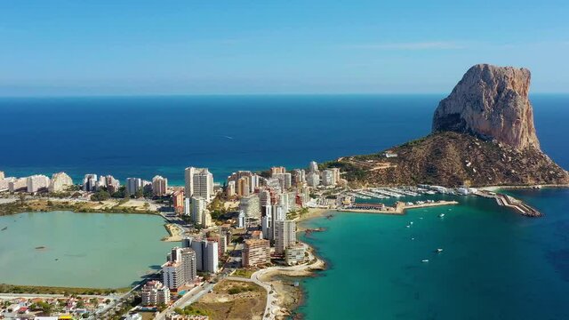 Aerial view with a drone of a beach in Calp city, Spain. Buildings are close to the beach full of tourists with Penyal d'Ifac Natural Park in the background  - aerial view with a drone 4K