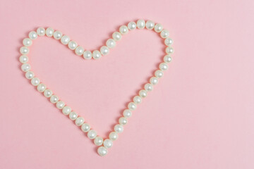 Pearl beads in the shape of heart on pink background with copy space. Valentines day concept. Greeting card template.