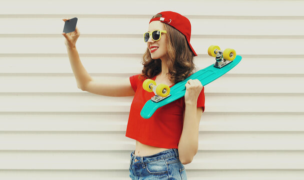 Portrait of happy smiling woman taking a selfie picture by phone with skateboard on a white background