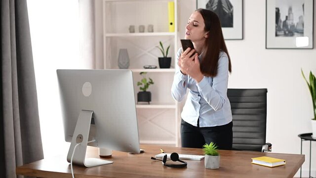 A female office employee in formal shirt is talking on the smartphone and typing on the PC keyboard, cheks smth. A young businesswoman talking on the phone working with a computer in the office