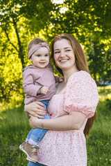 Fototapeta premium A young mother walks with a one-year-old baby, holds him in her arms, hugs. Communication with the child for his harmonious development